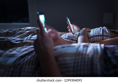 Bored distant couple ignoring each other lying in bed at night while using mobile phones. Smartphone addict. Obsessed and distracted man and woman texting. Addiction to social media and technology. - Powered by Shutterstock