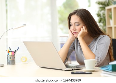 Bored entrepreneur woman looking at laptop screen sitting on a desk at home