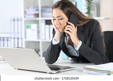 Bored executive calling on smart phone waiting on hold sitting on her desk at the office