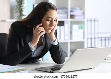 Bored executive with laptop waiting calling on smart phone sitting on her desk at office