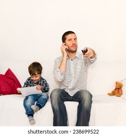 Bored Father Making A Phone Call And Watching Tv While Baby Is Playing With Tablet On A White Sofa With A Red Pillow And A Bear Toy