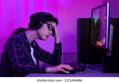 Bored Female Gamer Playing Video Games On Computer, Having Headache And Touching Forehead