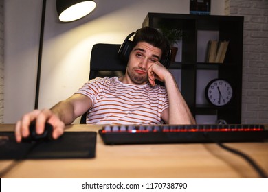 Bored Gamer Playing Video Games On Computer While Sitting By The Table At Home