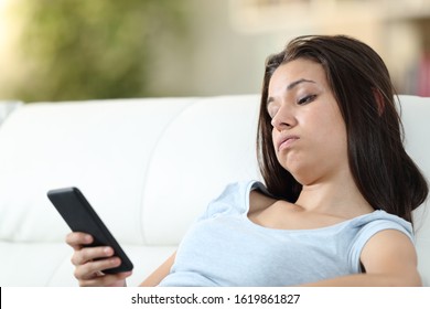 Bored girl checking mobile phone sitting on a couch in the living room at home