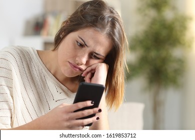 Bored Girl Holding Smart Phone Sitting On A Couch In The Living Room At Home