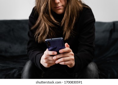 Bored Girl Using Her Smart Phone Sitting On A Couch In The Living Room At Home