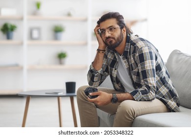 Bored Indian Guy Sitting On Couch With Joystick, Looking At Copy Space, Playing Video Games Alone At Home. Middle-eastern Young Man Feeling Lonely While Spending Weekend Alone, Home Entertainment