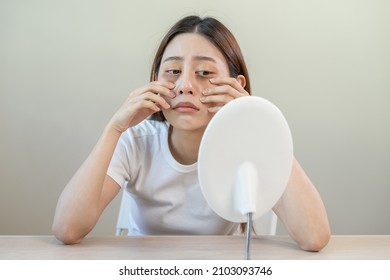 Bored, insomnia asian young woman, girl looking at mirror, without makeup, touch under eyes with problem of dark circles, puffiness, swollen or wrinkles on face. Sleepless, sleepy people, copy space - Shutterstock ID 2103093746