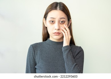 Bored, insomnia asian young woman, girl looking at camera, hand touching under eyes with problem of black circles or panda puffy, swollen and wrinkle on face. Sleepless, sleepy healthcare person. - Shutterstock ID 2212293603