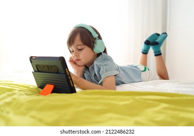 Bored little boy looking at tablet with sad face lying down on sofa looking deep in thought. Child using electronic devices while slouching on bed at home. Loneliness modern childhood. - Shutterstock ID 2122486232