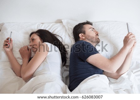 Bored lovers couple in bed and using  mobile phone 