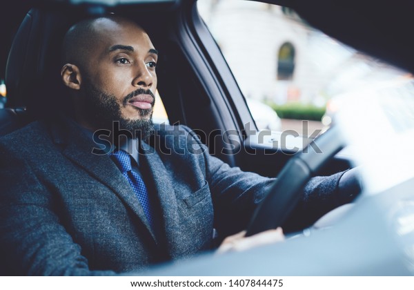 Bored male executive entrepreneur dressed in formal\
clothing driving to office destination feeling tired from long day\
in enterprise, serious man holding hands on steering wheel and\
looking on road
