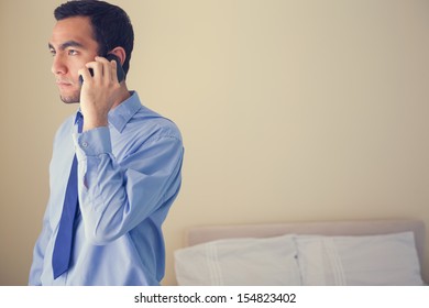 Bored man calling someone with a mobile phone and looking away in a bedroom at home