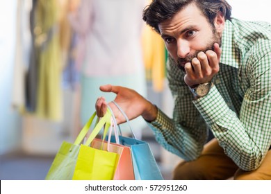 Bored Man With Shopping Bags While Woman By Clothes Rack In A Shop