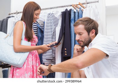 Bored man sitting and consulting wristwatch in front of his woman at a boutique - Powered by Shutterstock