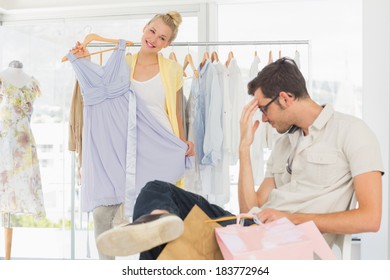 Bored Man Sitting With Shopping Bags While Woman Selecting Dress In The Background