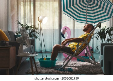 Bored man spending summer vacations at home and pretending he is on the beach, he is sunbathing in his living room and resting on a deckchair