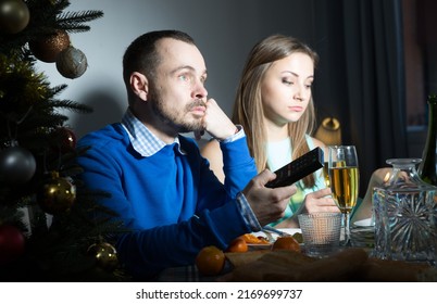 Bored Man And Woman Sitting At Dining Table During Festive Dinner At Christmas Night