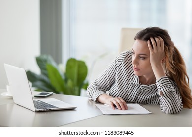 Bored millennial female worker lie at office desk look at laptop screen think about problem solution, unmotivated businesswoman search inspiration, tired of monotonous work. Lack of motivation concept