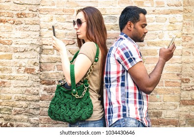 Bored multiracial couple using mobile smart phone - Addiction isolation concept with millennials young people using smartphone - Boyfriend and girlfriend on disinterest moment - Warm neutral filter