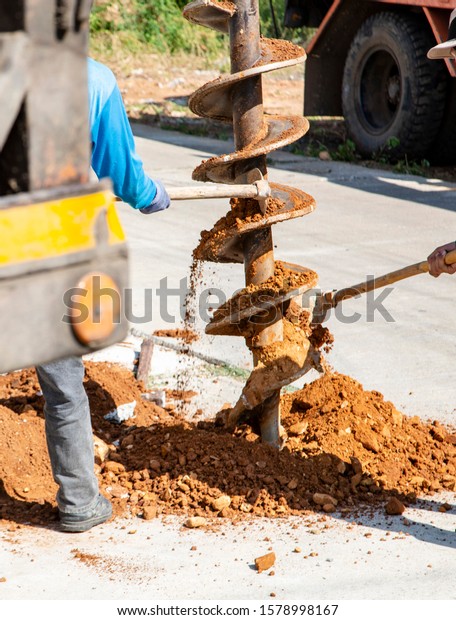 Bored Pile Hydraulic Is a car for\
devices that have Drill bit, drill down  on the ground,  drill,\
male worker is using hoe Scraping the soil from the drill\
bit.