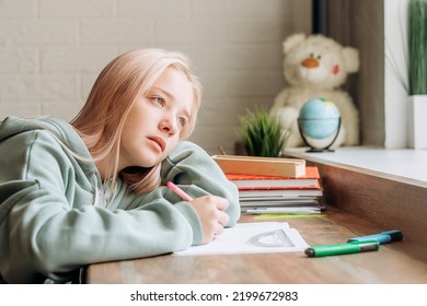 Bored pretty blonde teenage girl in home clothes doing homework,making notes in notebook at home at her desk.School concept. - Powered by Shutterstock