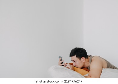 Bored And Sad Asian Man Using Mobile Phone And Relaxed On Beanbag Sofa.