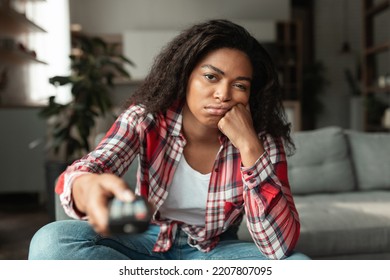 Bored Sad Pretty Millennial African American Female With Remote Control, Watch Tv News Or Movie, Sitting On Sofa In Living Room Interior, Free Space. Leisure Time, Idleness At Home And People Emotions