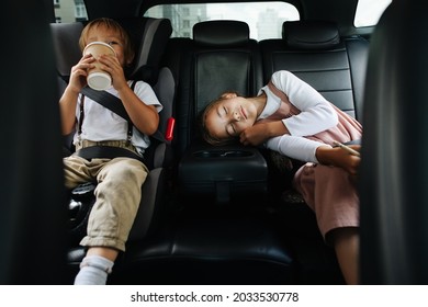 Bored siblings riding on a back seat in a car. View from inside salon. Boy is drinking from plastic cup, girl is napping. - Shutterstock ID 2033530778