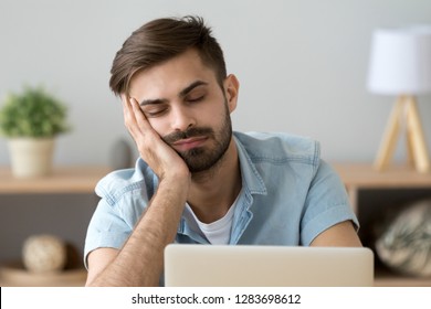 Bored sleepy man feels tired drowsy resting on hand near laptop, unmotivated lazy sluggish office worker disinterested in dull work boring monotony routine wasting time, boredom lack of sleep concept