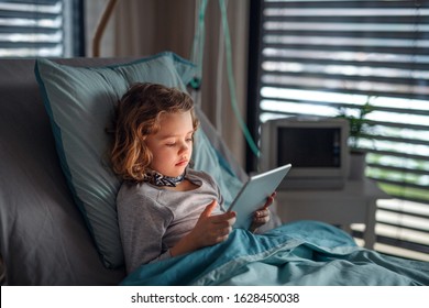 Bored small girl in bed in hospital, using tablet to pass time. - Powered by Shutterstock