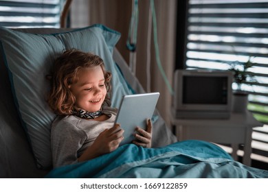 Bored small girl in bed in hospital, using tablet to pass time. - Powered by Shutterstock