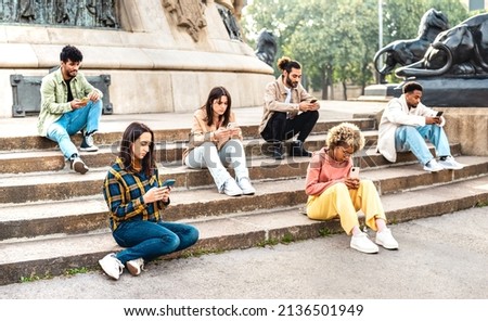 Bored students group using mobile smart phone sitting at university college yard - Young friends addicted by smartphone devices - Technology concept with always connected people on bright vivid filter