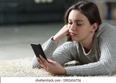 Bored teen checking smart phone lying on the floor at home