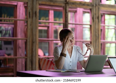 Bored unhappy caucasian girl student look at laptop with hand near head sit at desk in library or coworking space. Female thinking of something, pensive abstracted not concentrated on online lesson