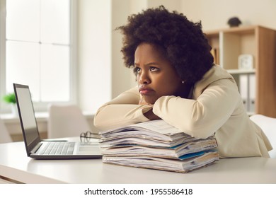 Bored unsatisfied young woman waiting for working day to end. Tired employee dissatisfied she has to work extra hours and do all paperwork sitting at office desk pouting lips with sad face expression