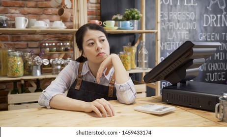 Bored Waitress Girl In Apron Sitting In Cafe Bar Counter With Hand In Chin Looking Out Store. Depressed Coffee Shop Owner With No Customer Visiting. Unhappy Lady Worried About Small Startup Business