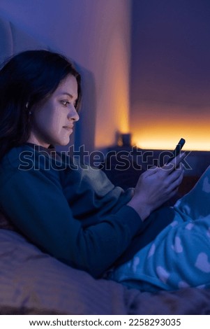 Bored woman chatting and surfing on internet with smartphone late at night, lying on bed