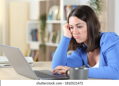 Bored woman checking laptop online content sitting on a desk at home