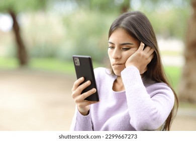Bored woman checks smart phone sitting in a park
