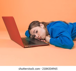 Bored Woman With A Laptop. Tired Woman  Orange Background. 20-22 Years Old Caucasian Woman.