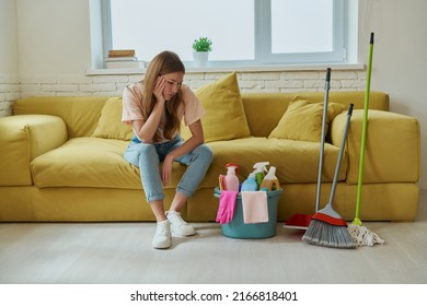 Bored Woman Looking At The Bucket With Cleaning Products While Sitting On The Couch At Home