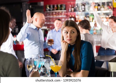 Bored Woman Sitting At Table Among Dancing Colleagues At Corporate Party