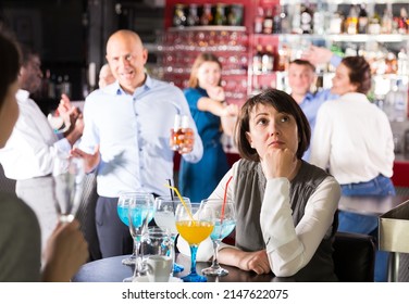 Bored Woman Sitting At Table Among Dancing Colleagues At Corporate Party