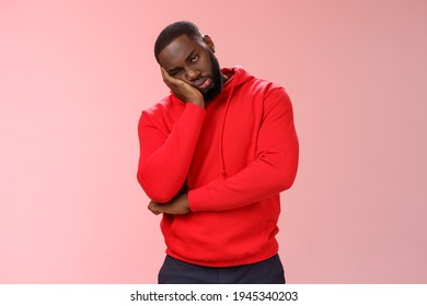 Bored young 25s black guy in red hoodie facepalm lean head hand look indifferent sleepy attend boring meeting fall asleep carelessly listening uninteresting story, pink background
