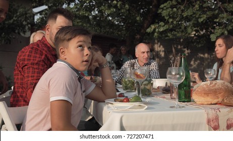 Bored Young Boy Feeling Annoyed Sitting At Table On Family Reunion Party.