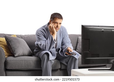 Bored Young Man In A Bathrobe Watching Tv And Sitting On A Sofa Isolated On White Background