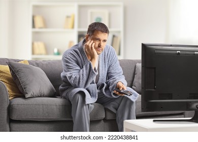 Bored Young Man In A Bathrobe Watching Tv And Sitting On A Sofa At Home