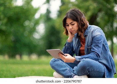 Bored Young Middle Eastern Female Student Sitting With Digital Tablet On Bench Outdoors, Upset Millennial Arab Woman Looking At Pad Computer Screen While Resting Outside In Park, Copy Space