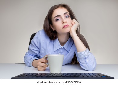 Bored Young Woman With Coffee Cup Sitting At Grey Office Desktop With Computer Keyboard